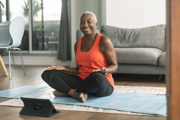 A senior black woman participates in a virtual fitness class from home