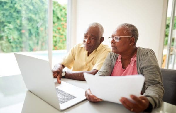 Shot of a senior african couple with a paper looking at a laptop at home