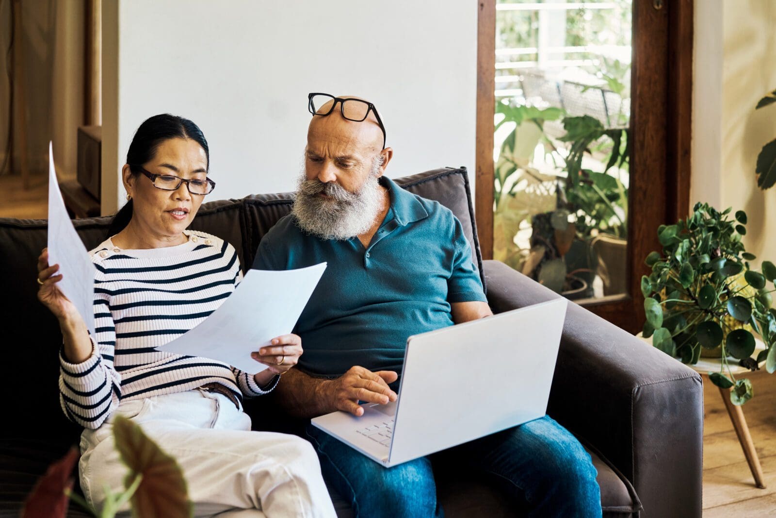 man and woman reviewing documents on couch with laptop