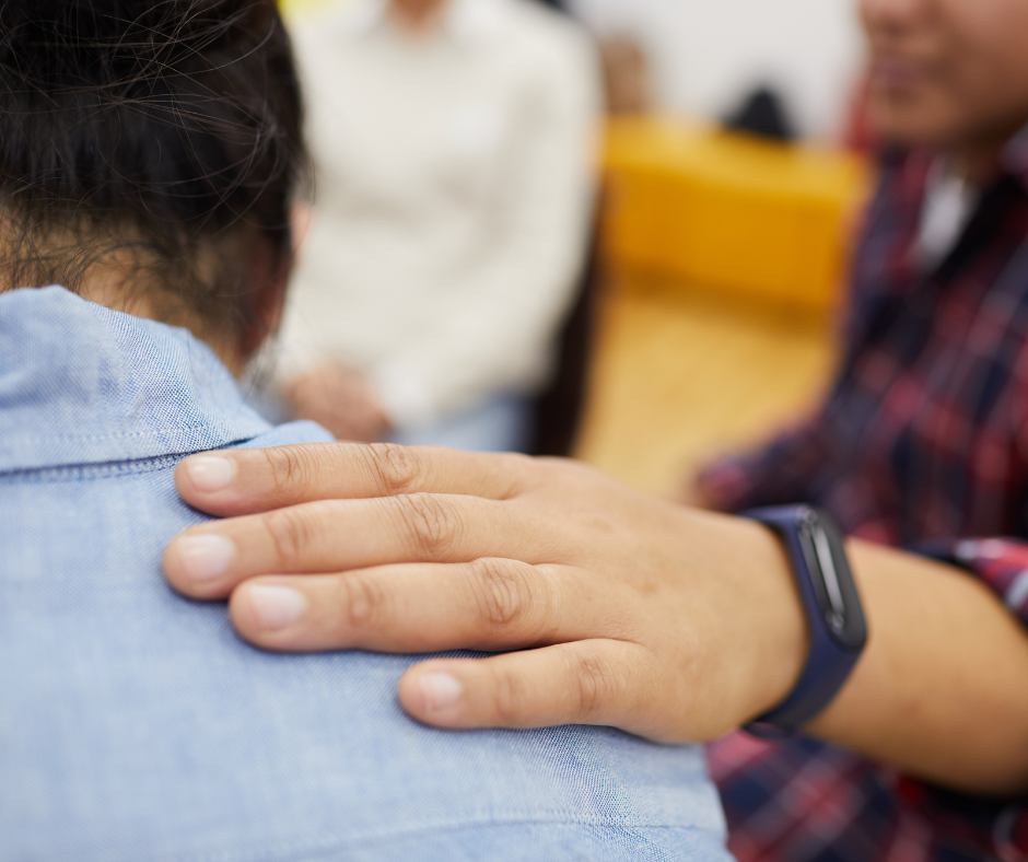 Closeup of a hand on a person's shoulder, offering comfort during a support group.